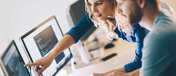 A young male looks at a computer screen while a young woman points to something on the screen.